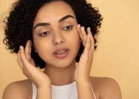 Close-up of a woman applying under-eye mask in a studio setting, focusing on skincare and wellness.